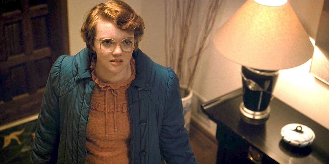 Shannon Purser als Barbara Holland, Brille und blauer Mantel, in einem Eingang.